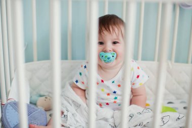 Küçük oğlan ışık odasında beşiğinde oturuyor ve oyuncaklarıyla oynuyor.