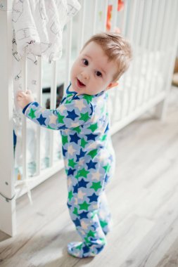 Küçük bebek, ışık odasında beşiğinin yanında duruyor ve küçük kediciğiyle oynuyor.