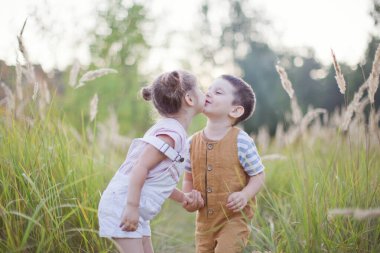 Küçük oğlan ve kız gün batımında tarlada oynuyorlar. Tatlı erkek ve kız kardeşler.