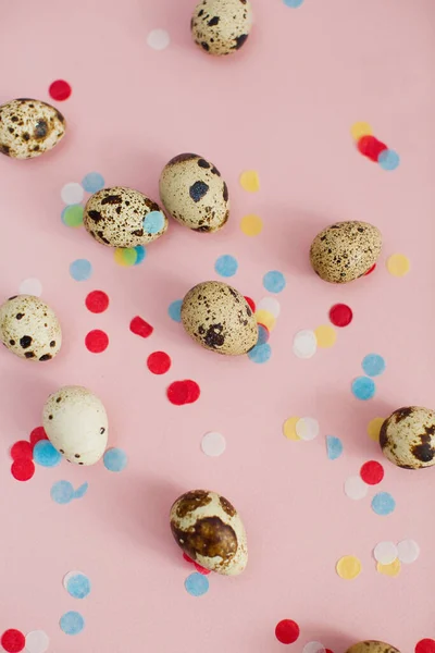 Quail eggs on a pink background with colorful confetti. Easter eggs