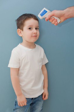 Genç adam mavi arka planda bir çocuğun vücut ısısını ölçüyor.