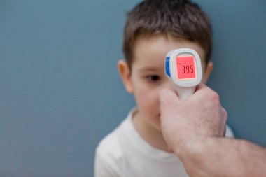 Mavi arka planda çocuğun vücut ısısını ölçmek için kızılötesi termometre kullanılıyor.