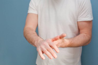 Ameliyat maskesi takan genç adam mavi arka plandaki mikroplardan ellerini temizlemek için el dezenfektanı kullanıyor.