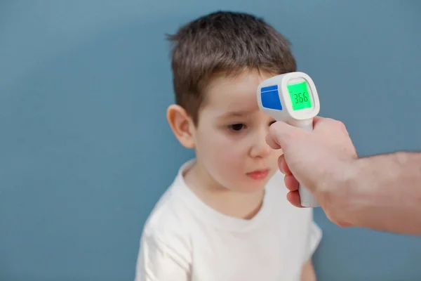 using infrared thermometer to measure child\'s body temperature on a blue background