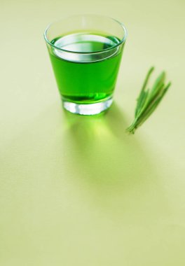 Yeşil organik buğday suyu ve yeşil ahşap kutunun içindeki yeşil çimen sarı arka planda.