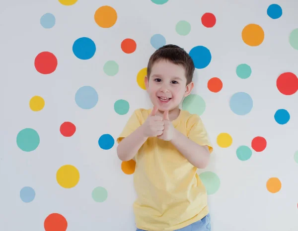 Maluch Biały Chłopiec Tle Ściany Kolorowymi Kółkami Chłopiec Daje Kciuki — Zdjęcie stockowe