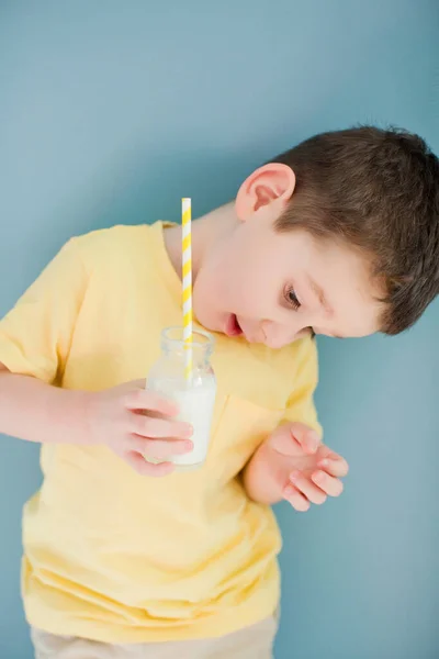 Toddler caucasian boy in a yellow t-shirt drink milk from glass bottle and straw