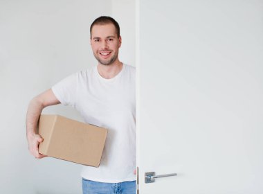 Karton kutulu beyaz bir adam kapıyı açar ve odaya girer. Beyaz arka planda teslimatçı.