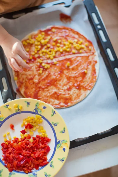 Child make vegan pizza with corn and red pepper. Little helper and homemade pizza