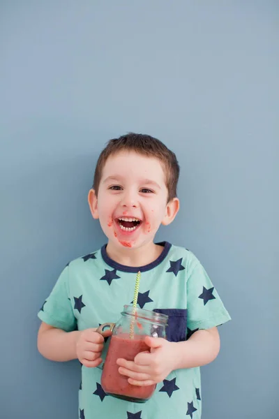 可愛いです幼児男の子飲む健康スムージーからガラスメイソンジャー上の青の背景 — ストック写真