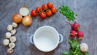 Gri arka planda taze sebzeli kompozisyon, metin için boşluk. Çiğ taze sebzelerin yanında küçük boş tencere.