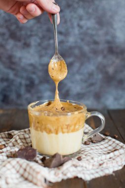 Buzlu Dalgona kahvesi, cam bardakta çikolata tozu. Moda yumuşacık kremalı kremalı kahve. Ahşap bir arka planda kahve.