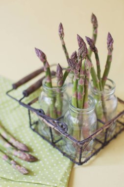 Sarı arka planda eski cam şişelerde taze çiğ yeşil kuşkonmaz.