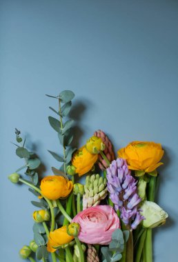 Turuncu ve pembe ranunculus çiçekleri, okaliptüs ve mavi arka planda sümbülü olan güzel bir buket. Mavi arkaplanda çiçekler ve metin için boşluk