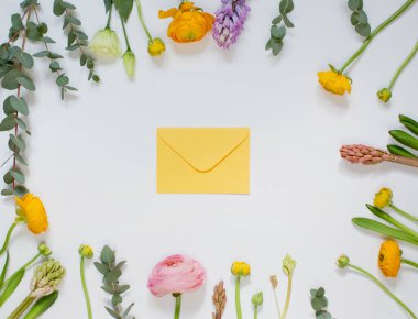 Pembe ve turuncu renkte çiçek çerçevesi, sümbül ve okaliptüs beyaz bir zemin üzerinde sarı bir zarf, üst görünüm.