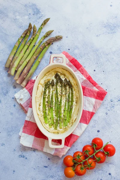 Pie with green asparagus and cream cheese in a baking form on a light blue background