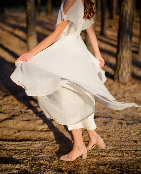 Young woman dancing in a white sparkle dress at sunset light