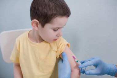 Aşı konsepti. Mavi eldivenli doktor klinikte sarı tişörtlü çocuğu aşılıyor.