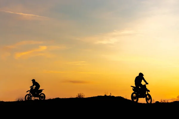 Two Black silhouette Motocross rider on a motorcycle in front of