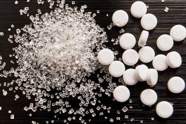 tatlandırıcı haplar koyu bir arka planda şekerle yatar.