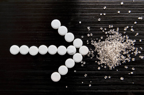 подсластитель таблетки лежат с сахаром на темном фоне
