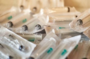 Bir paket açılmamış şırınga. Mühürlü şırıngalar desenli bir yüzeyde yatıyor..