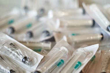 Bir paket açılmamış şırınga. Mühürlü şırıngalar desenli bir yüzeyde yatıyor..