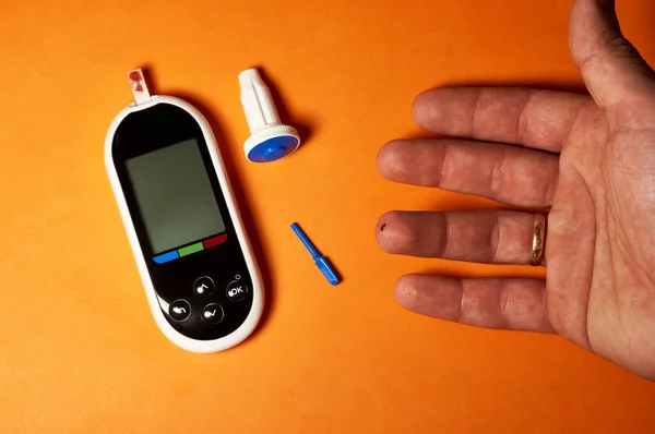A diabetic checks his blood sugar. Close up man hands self-tested with a Lancet and a glucometer at home