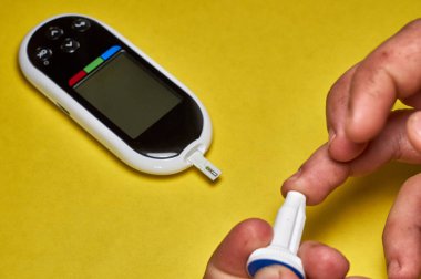 Şeker hastası kan şekerini ölçer. Erkek eli, evinde bir mızrak ve glukometreyle kendini test etti.