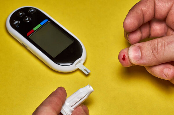 A diabetic checks his blood sugar. Close up man hands self-tested with a Lancet and a glucometer at home