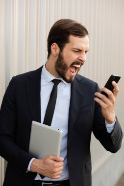 elegant man screeming at his cellphone outside clipart