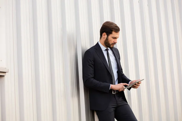 Homem elegante de pé contra uma parede cinza com um tablet — Fotografia de Stock