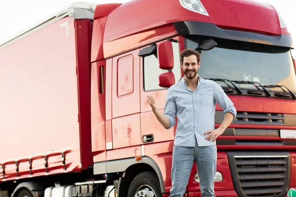 masculine truck driver in jeans with his truck behind