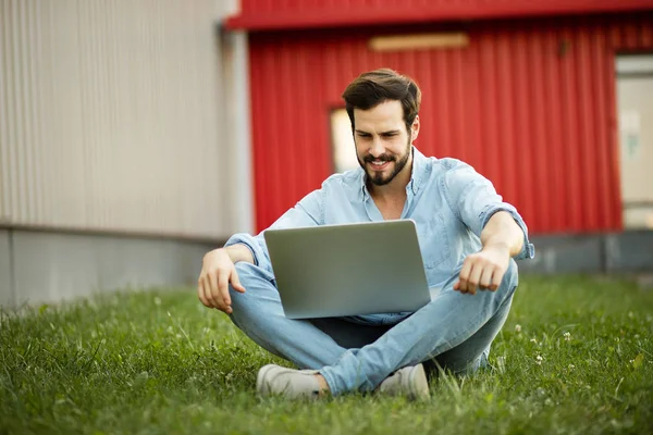Giovane uomo in jeans casual vestito sdraiato con il suo computer portatile in f — Foto Stock