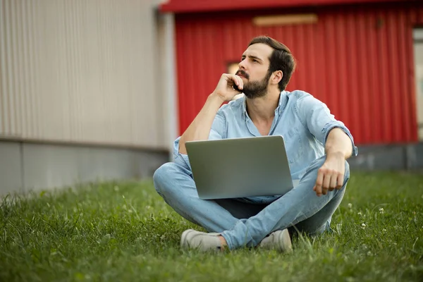Giovane uomo in jeans casual vestito sdraiato con il suo computer portatile in f — Foto Stock