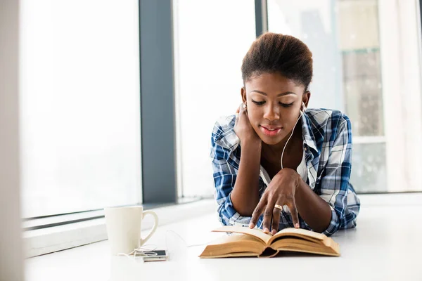 Mujer negra leyendo un libro al lado de una gran ventana con labio natural — Foto de Stock