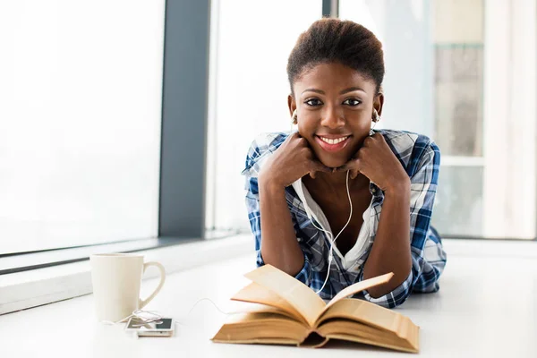 Mujer negra leyendo un libro al lado de una gran ventana con labio natural — Foto de Stock