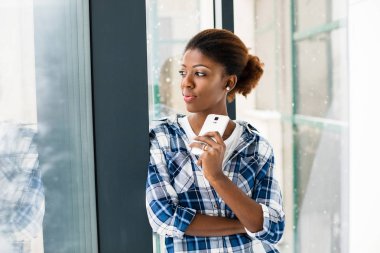 cep telefonunu kullanarak bir pencerenin yanındaki genç siyah kadın