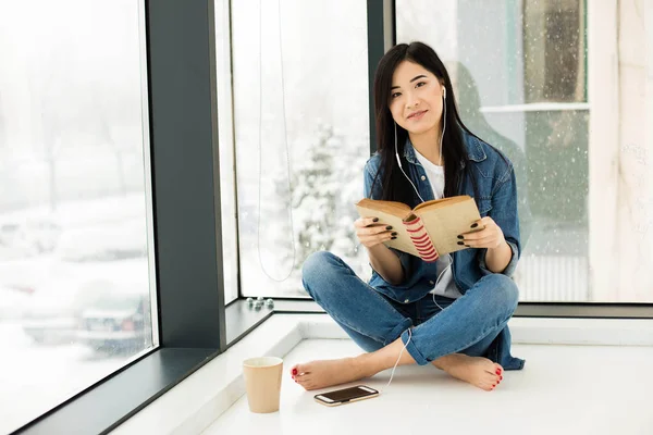 Mujer asiática leyendo un libro al lado de grandes ventanas — Foto de Stock