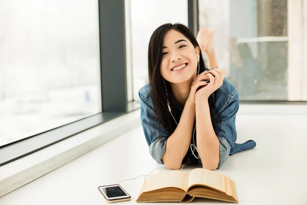 Asiatin liest ein Buch neben großen Fenstern — Stockfoto