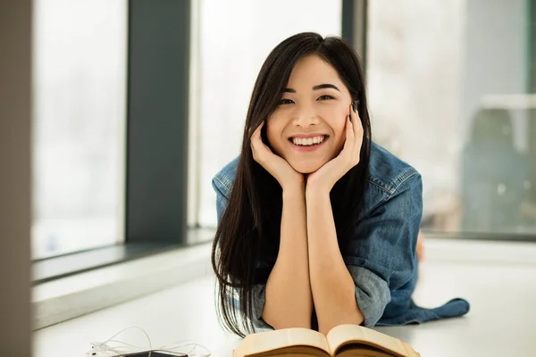 Mujer asiática leyendo un libro al lado de grandes ventanas — Foto de Stock