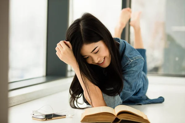 Mujer asiática leyendo un libro al lado de grandes ventanas — Foto de Stock