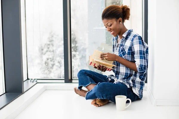 Mujer negra leyendo un libro al lado de una gran ventana con labio natural — Foto de Stock