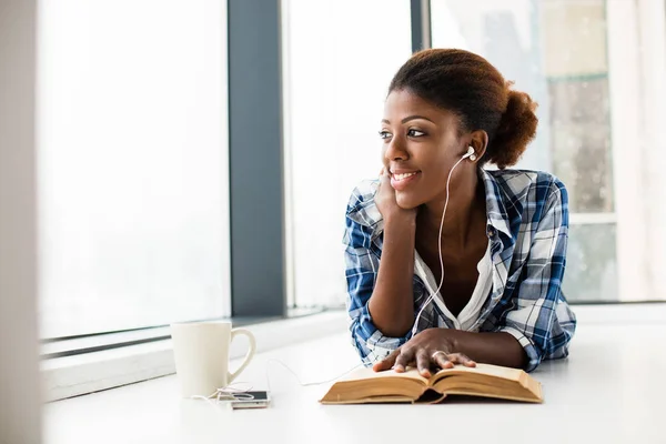 Mujer negra leyendo un libro al lado de una gran ventana con labio natural — Foto de Stock