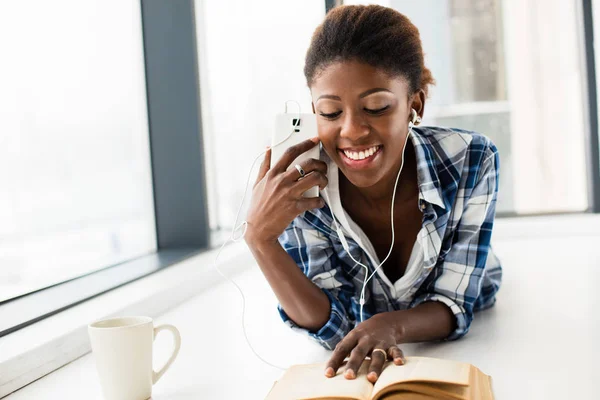 Mujer negra leyendo un libro al lado de una gran ventana con labio natural — Foto de Stock