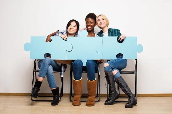 Skupina tří různých žen sedí v křeslech s puzzle — Stock fotografie
