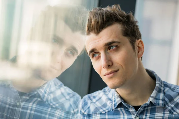 Młody człowiek w checkeret koszuli stojący obok okna — Zdjęcie stockowe