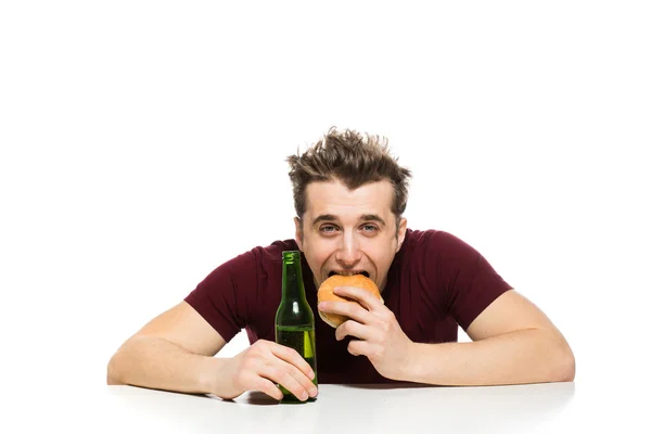 Junger Mann trinkt Bier und isst Hamburger — Stockfoto