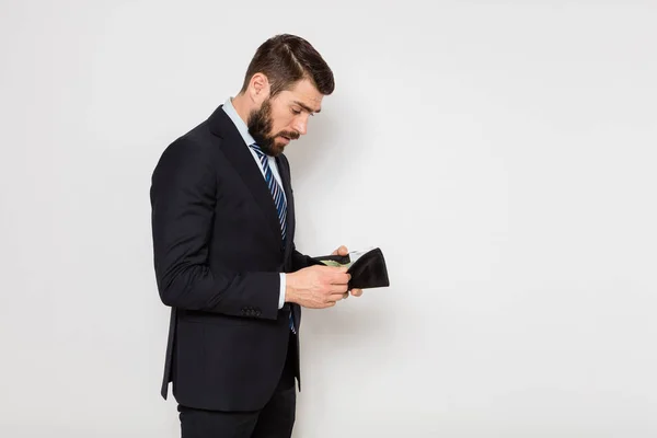 Eleganter Mann, der sein Portemonnaie auf weißem Hintergrund kontrolliert — Stockfoto