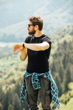 kayaların üzerinde duran ve saatini kontrol adam